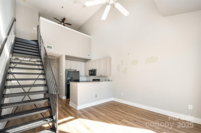 staircase with hardwood / wood-style floors, high vaulted ceiling, and ceiling fan