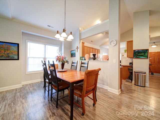 dining area with a chandelier, vaulted ceiling, and light hardwood / wood-style flooring