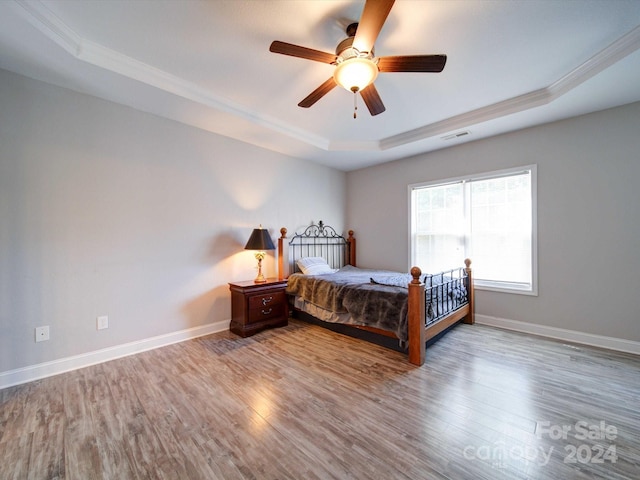 bedroom featuring light hardwood / wood-style flooring, a tray ceiling, crown molding, and ceiling fan