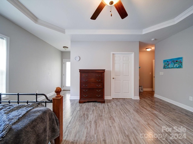 bedroom featuring light hardwood / wood-style flooring, ornamental molding, a tray ceiling, and ceiling fan