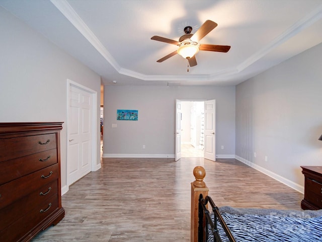 bedroom with ceiling fan, crown molding, a tray ceiling, and light hardwood / wood-style floors