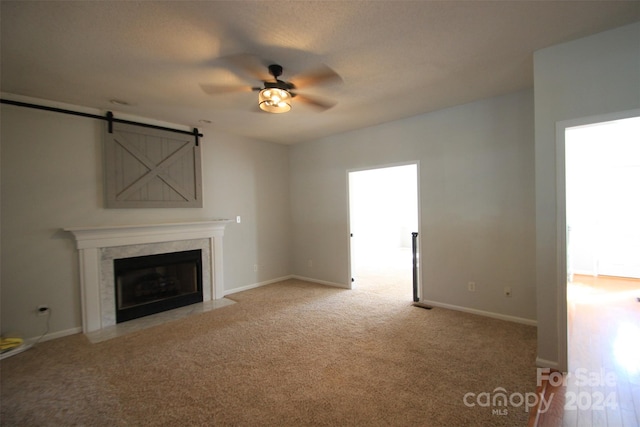 unfurnished living room featuring a barn door, a high end fireplace, light carpet, and ceiling fan