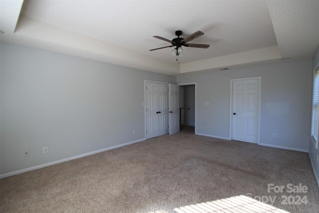 unfurnished bedroom with light carpet, ceiling fan, a tray ceiling, and two closets