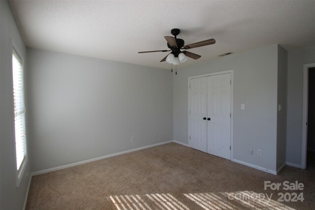 unfurnished bedroom with ceiling fan, a textured ceiling, a closet, and carpet flooring