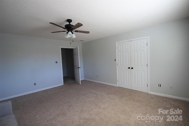 unfurnished bedroom with a closet, light colored carpet, a textured ceiling, and ceiling fan