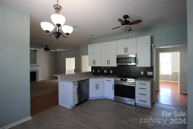 kitchen featuring dark hardwood / wood-style floors, stainless steel appliances, white cabinets, kitchen peninsula, and decorative light fixtures