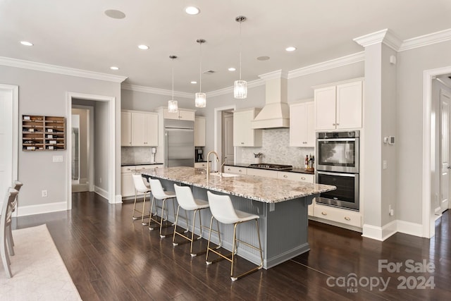 kitchen featuring dark wood-type flooring, a center island with sink, decorative light fixtures, custom exhaust hood, and appliances with stainless steel finishes