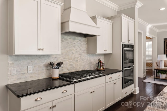 kitchen with appliances with stainless steel finishes, white cabinets, custom range hood, crown molding, and dark wood-type flooring