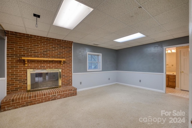 unfurnished living room with carpet, a drop ceiling, and a brick fireplace