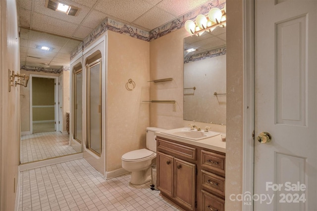 bathroom featuring a paneled ceiling, walk in shower, toilet, vanity, and tile patterned flooring