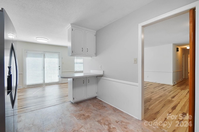 kitchen with white cabinets, stainless steel fridge, kitchen peninsula, a textured ceiling, and light hardwood / wood-style floors