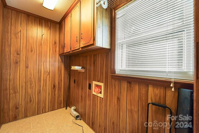 washroom featuring hookup for a washing machine, cabinets, wooden walls, and a textured ceiling