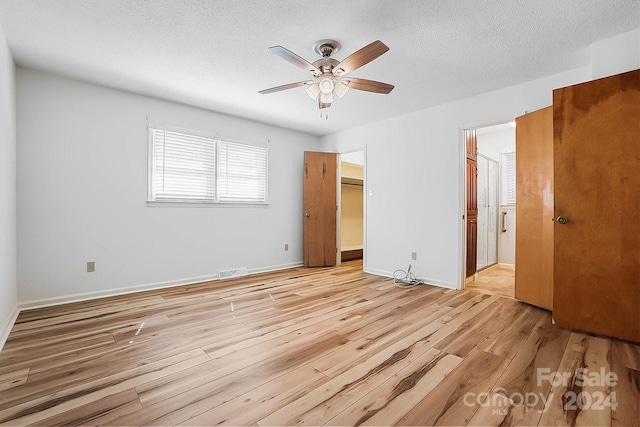 unfurnished bedroom with ceiling fan, a textured ceiling, light hardwood / wood-style floors, and a spacious closet