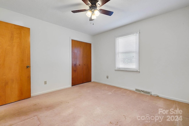 unfurnished bedroom featuring ceiling fan, light colored carpet, and a closet