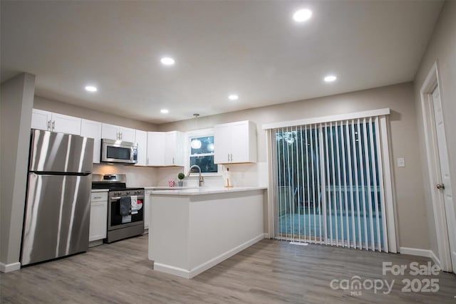 kitchen featuring kitchen peninsula, stainless steel appliances, white cabinetry, and light hardwood / wood-style flooring
