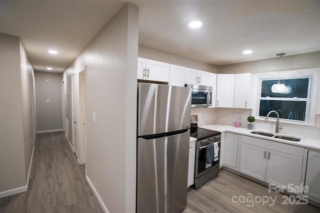 kitchen featuring pendant lighting, white cabinets, sink, light wood-type flooring, and stainless steel appliances