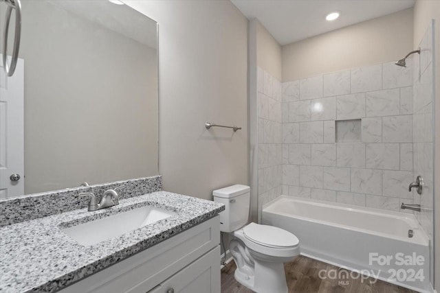 full bathroom with wood-type flooring, tiled shower / bath, vanity, and toilet