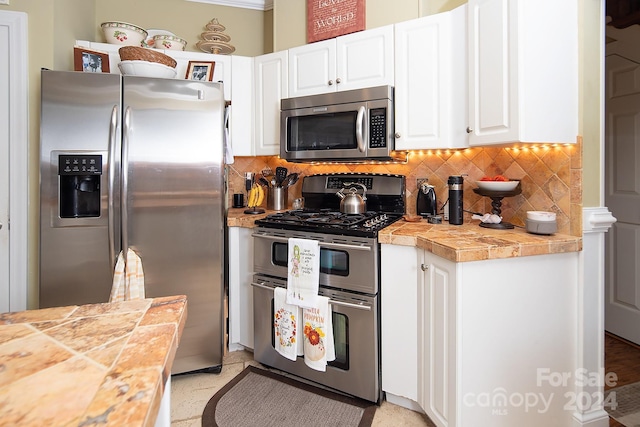 kitchen with appliances with stainless steel finishes, tile countertops, white cabinetry, and decorative backsplash