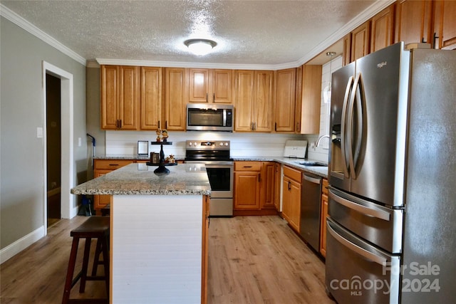 kitchen with a breakfast bar area, a kitchen island, light wood-type flooring, crown molding, and stainless steel appliances