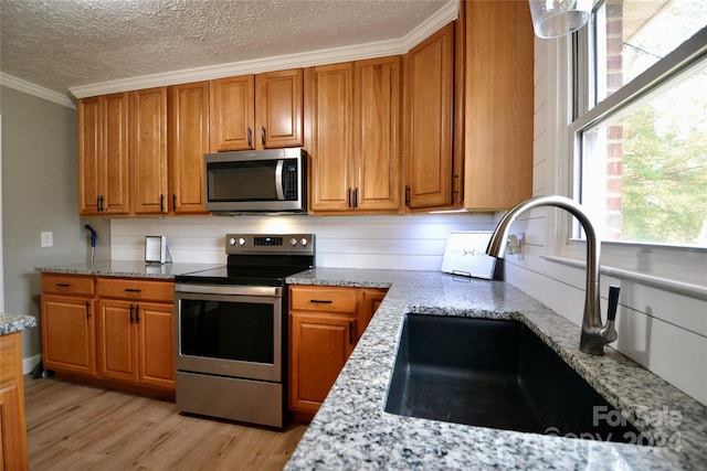 kitchen with sink, light stone countertops, crown molding, light wood-type flooring, and appliances with stainless steel finishes