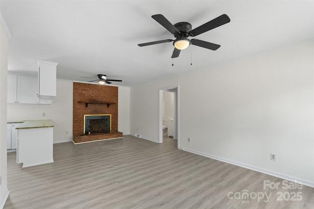 unfurnished living room with a brick fireplace, light wood-style flooring, and baseboards