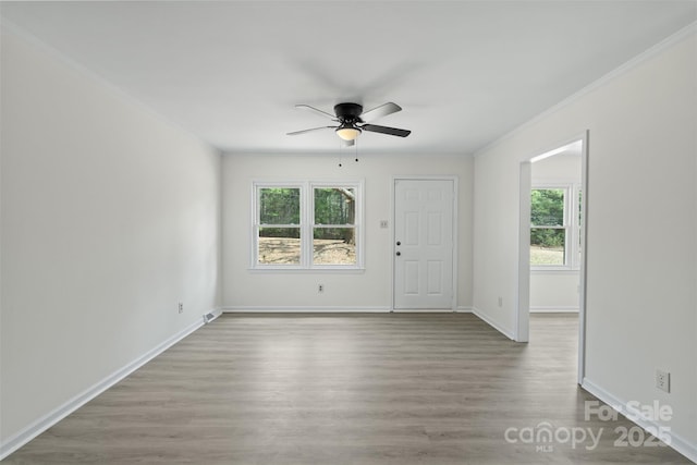 spare room featuring plenty of natural light, wood finished floors, baseboards, and ornamental molding