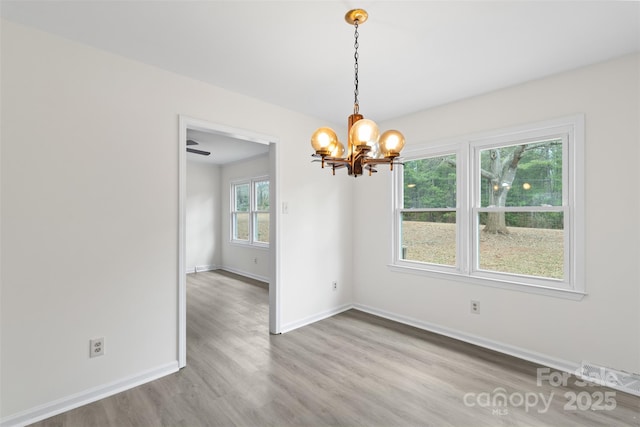 unfurnished dining area with a notable chandelier, visible vents, baseboards, and wood finished floors