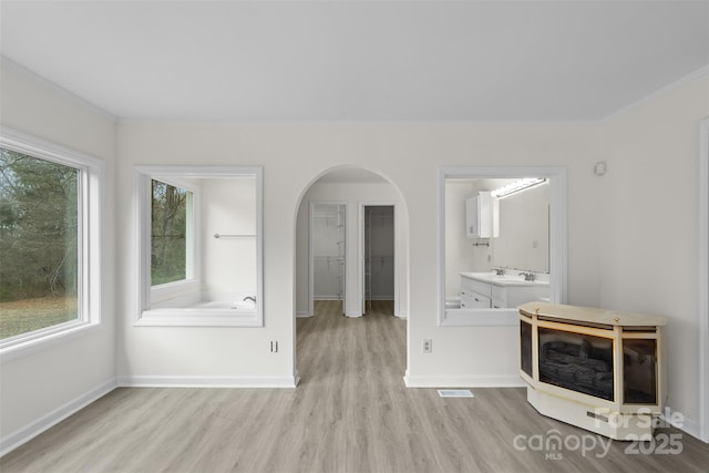 unfurnished living room with arched walkways, light wood-style floors, a healthy amount of sunlight, and crown molding