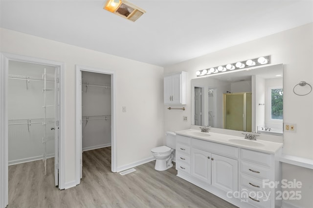 full bathroom with visible vents, double vanity, a stall shower, wood finished floors, and a sink