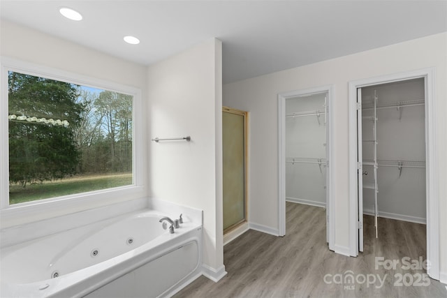 bathroom with a walk in closet, a stall shower, a jetted tub, wood finished floors, and baseboards