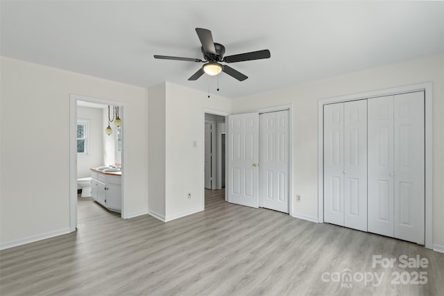 unfurnished bedroom featuring baseboards, light wood finished floors, ensuite bath, a sink, and multiple closets