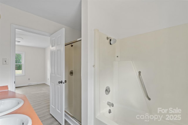 full bath featuring combined bath / shower with glass door, a sink, visible vents, and wood finished floors