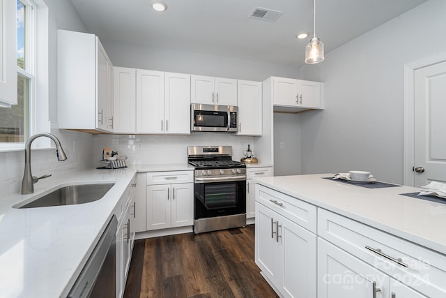 kitchen with white cabinets, hanging light fixtures, sink, stainless steel appliances, and dark hardwood / wood-style floors