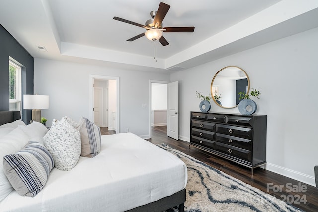 bedroom with ceiling fan, dark wood-type flooring, and a tray ceiling