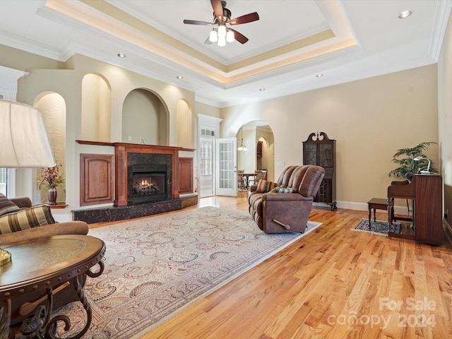 living room featuring a fireplace, a raised ceiling, light hardwood / wood-style floors, ceiling fan, and ornamental molding