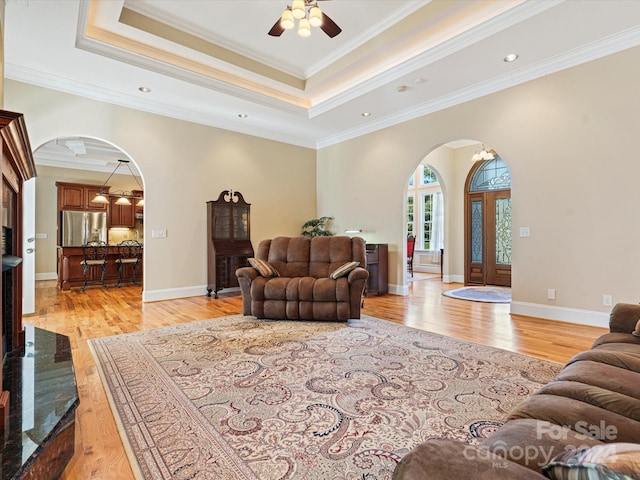 living room featuring crown molding, light hardwood / wood-style flooring, a tray ceiling, and ceiling fan