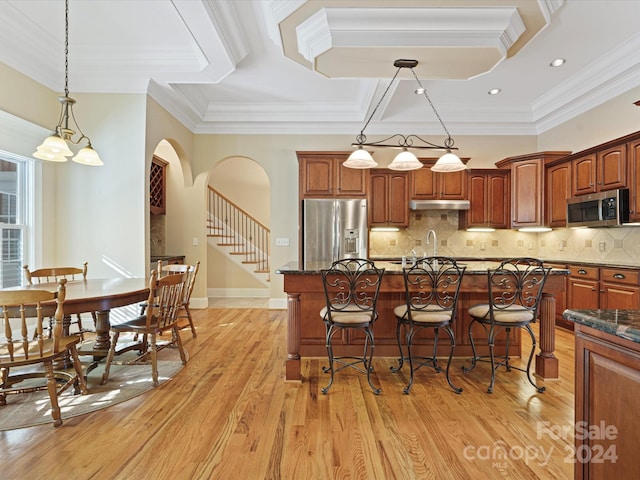 kitchen featuring hanging light fixtures, crown molding, a center island, appliances with stainless steel finishes, and light hardwood / wood-style floors