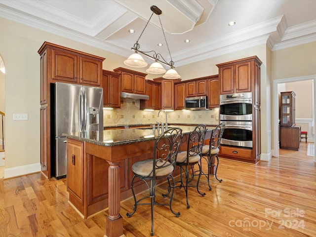 kitchen with an island with sink, stainless steel appliances, dark stone countertops, ornamental molding, and light hardwood / wood-style floors