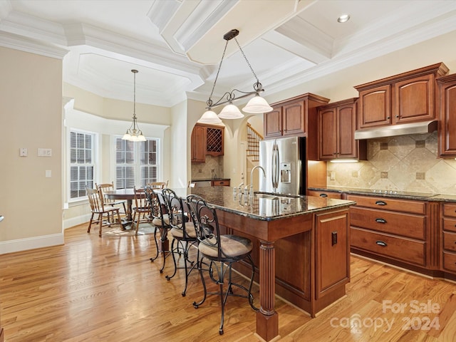 kitchen featuring stainless steel fridge, light wood-type flooring, pendant lighting, and an island with sink