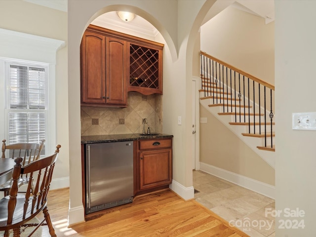 bar with backsplash, stainless steel refrigerator, dark stone countertops, light hardwood / wood-style floors, and crown molding