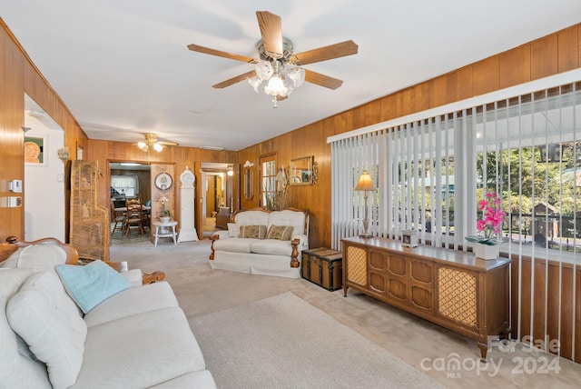 living room featuring ceiling fan, light colored carpet, and wooden walls