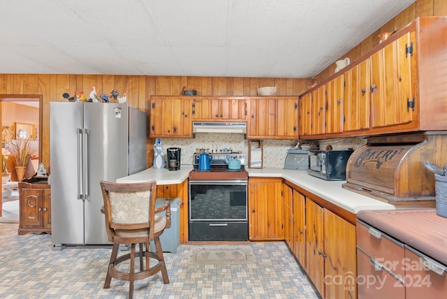 kitchen featuring electric stove, stainless steel fridge, wood walls, and decorative backsplash