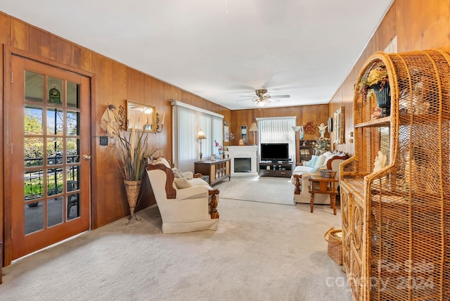 living room featuring ceiling fan, wood walls, and light colored carpet