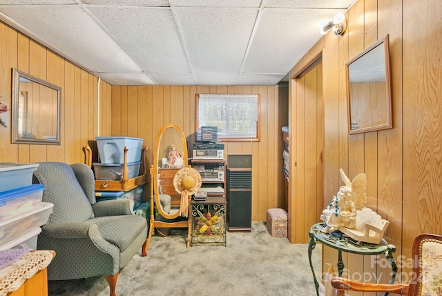 living area with light colored carpet, wooden walls, and a drop ceiling