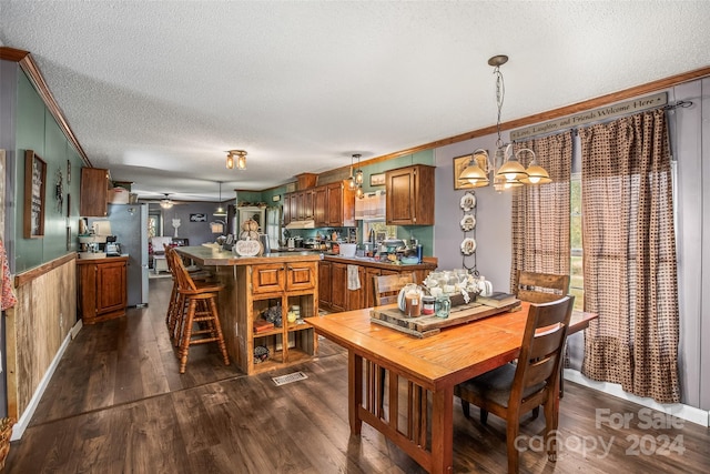 dining area featuring wood walls, dark hardwood / wood-style floors, ornamental molding, a textured ceiling, and ceiling fan