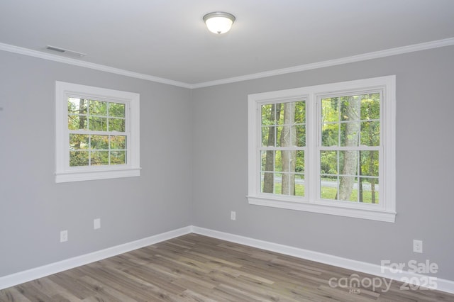 empty room with hardwood / wood-style flooring, crown molding, and a wealth of natural light