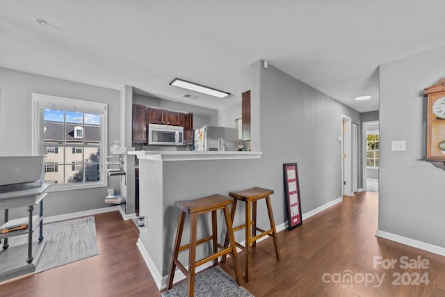 kitchen with appliances with stainless steel finishes, a breakfast bar area, kitchen peninsula, and dark hardwood / wood-style floors