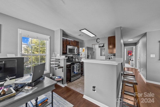 kitchen with kitchen peninsula, appliances with stainless steel finishes, a kitchen bar, light hardwood / wood-style floors, and sink