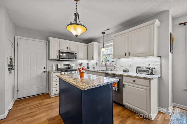 kitchen with a center island, white cabinetry, stainless steel appliances, decorative light fixtures, and light hardwood / wood-style flooring