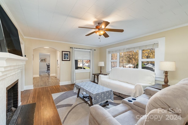 living room featuring hardwood / wood-style flooring, a brick fireplace, ceiling fan, and ornamental molding